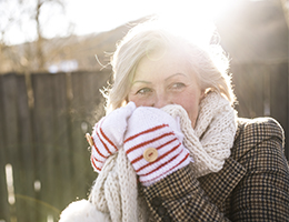 A woman sitting outside and wearing a coat, gloves and scarf