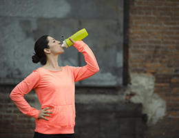 A woman standing outside in athletic gear takes a break to drink from her water bottle.