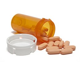 Light orange tablets tumble out of an overturned orange medicine bottle. A white cap sits beside them. 